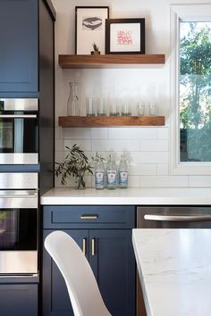 a modern kitchen with blue cabinets and white counter tops is pictured in this image, there are shelves on the wall above the stove