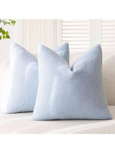 two light blue pillows sitting on top of a white couch next to a plant in a vase