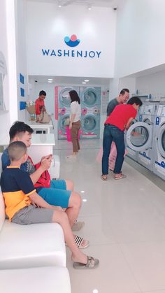 two boys sitting on a white couch in front of washers and dryer machines