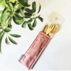 utensils in a pink pouch next to a potted plant on a white surface