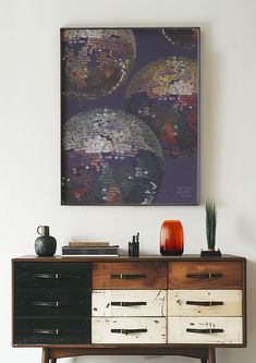 an art work hangs on the wall next to a dresser with drawers and vases