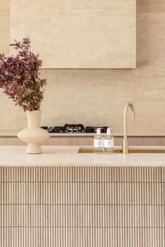 A kitchen features brushed brass tapware and travertine stone feature tiles. Tiled Island Bench Kitchen, Travertine Benchtop, Brass Benchtop, Fluted Travertine, Organic Brutalism, Dubai Townhouse, Microcement Kitchen, Travertine Kitchen, Travertine Countertops