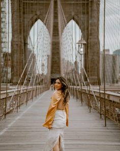 a woman standing on a bridge in front of the brooklyn bridge wearing a tan leather jacket