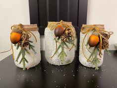 three mason jars decorated with pine cones and ornaments