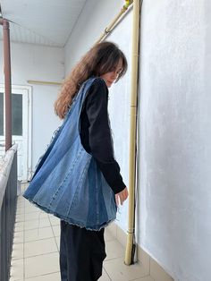 a woman with long hair wearing a blue jean jacket and black pants standing in front of a white wall