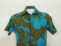 "Vintage 1960s op art Hawaiian shirt. Made of cotton. Color is electric blue and green/brown with hibiscus flowers like Warhol's poppies. Shirt has a button front, top button loop and single matching pattern chest pocket. Made by Hawaiian Casuals. Made in Hawaii. Size small. Measurements are: 39\" at the chest 39\" at the waist 15.5\" shoulder seam to shoulder seam 28\" overall length In very good condition." Green Collared Hawaiian Shirt With Floral Print, Green Retro Print Shirt For Spring, Vintage Green Cotton Hawaiian Shirt, Retro Patterned Cotton Hawaiian Shirt, Retro Fitted Hawaiian Shirt For Spring, Vintage Short Sleeve Shirt With Hibiscus Print, Retro Cotton Hawaiian Shirt With Tropical Print, Spring Vintage Hawaiian Shirt With Retro Print, Retro Blue Cotton Hawaiian Shirt