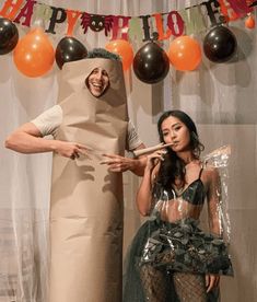 two people in costumes standing next to each other with balloons on the wall behind them