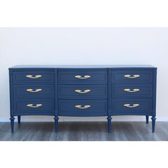 a large blue dresser with gold handles and drawers on the bottom, in front of a white wall