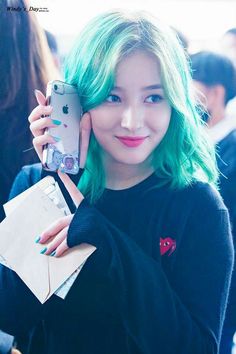 a girl with green hair is holding up her cell phone