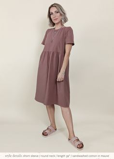 a woman standing in front of a white background wearing a brown dress and pink slippers