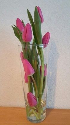 pink tulips in a clear glass vase on a wooden table against a white wall