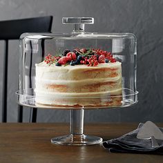 a cake sitting on top of a wooden table under a glass dome covered in berries