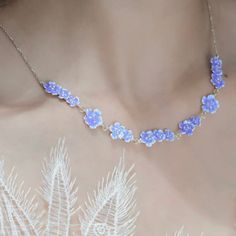 a woman wearing a necklace with blue flowers on it's neck and an attached chain