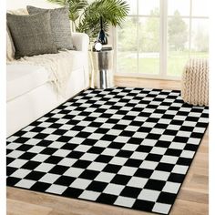 a black and white checkered area rug in a living room with couches, windows, and potted plant