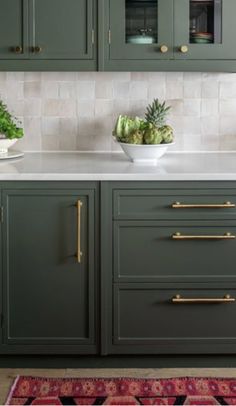 a kitchen with green cabinets and white counter tops, gold pulls on the handles to match the cabinetry