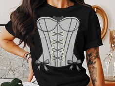 Elevate your style with this striking corset adorned with a captivating bat motif and accentuated by sleek black bows.  This classic unisex jersey short sleeve tee fits like a well-loved favorite. Soft cotton and quality print make users fall in love with it over and over again. These t-shirts have-ribbed knit collars to bolster shaping. The shoulders are tapered for a better fit over time. Dual side seams hold the garment's shape for longer.  .: Made with 100% Airlume combed and ring-spun cotton, a lightweight fabric (4.2 oz/yd² (142 g/m that is easy to layer, breathable. Perfect for active and leisure wear.  .: The retail fit that is perfect for casual and semi-formal settings. The crew neckline adds a classic, neat style that's perfect for accessorizing. .: Bella+Canvas manufactures all Fitted Graphic Print T-shirt For Costume Party, Edgy Black Tops For Costume Party, Fitted Graphic Print Tops For Costume Party, Edgy Black Top For Costume Party, Fitted Black T-shirt For Halloween, Black Crew Neck Top For Costume Party, Fitted Short Sleeve Tops For Costume Party, T Shirt Corset, Grey Corset