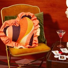 a chair with a heart pillow on it next to a table with wine glasses and other items