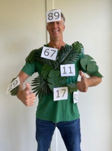 a man in a green shirt with numbers on his face and palm leaves around his shoulders