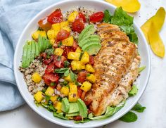 a white bowl filled with chicken, rice and veggies on top of a table