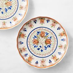 two plates sitting on top of a white table next to each other with orange and blue designs