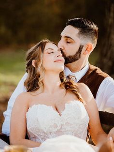 a bride and groom sitting at a table in front of a tree with their eyes closed