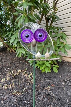 a purple glass owl sitting on top of a green plant in front of a house