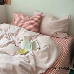 an open book laying on top of a bed with pink sheets and checkered pillows