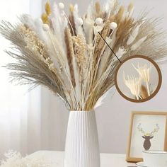 a white vase filled with dried flowers on top of a table next to a framed photo