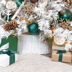 a white christmas tree with green and gold ornaments on it's branches, surrounded by presents