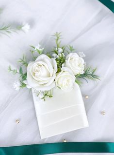 white roses and greenery are placed in a small box on top of a bed