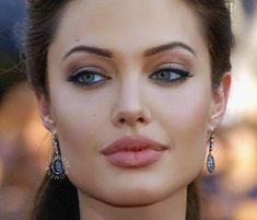 a close up of a woman wearing blue eyeshadow and earrings with her hair pulled back