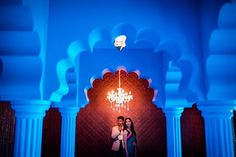 two people standing in front of a chandelier with blue lights on it and one person taking a photo