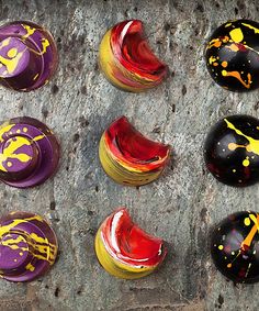 six painted rocks sitting on top of a cement slab with yellow and red paint splatters all over them