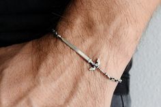 a man's arm with a silver bracelet and cross charm on it, against a white wall