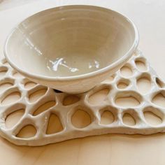 a white bowl sitting on top of a wooden table next to a plate with holes in it