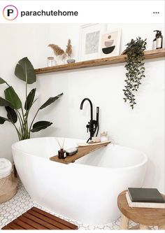 a white bath tub sitting in a bathroom next to a wooden stool and potted plant