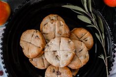 a black plate topped with cookies next to oranges and an olive sprig