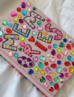 two pink notebooks covered in colorful magnets on a white sheet with a pillow behind them