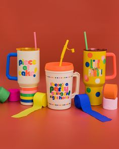 three colorful cups with straws and spoons next to each other on a pink background