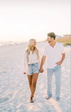 a man and woman walking on the beach holding hands