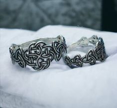 two silver rings sitting on top of a white cloth next to each other, one with an intricate design