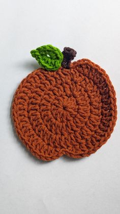 an orange knitted placemat with a green leaf on top