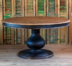 a round wooden table with black metal base on a wood floor in front of shutters