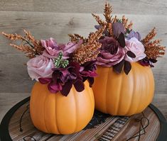 two pumpkins with flowers in them sitting on a wooden table next to each other