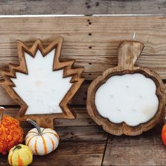 some pumpkins and gourds are sitting on a wooden table with maple leaf cutouts