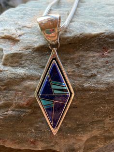 This beautifully well crafted Diamond shape Pendant has been handmade by a Navajo Artisan. The Colors of the Pendant come from Lapis Lazuli, Turquoise and Blue Opal. The Pendant measures 2.25” long and 3/4” wide. There are two pendants available and the design will vary. “Winds of Wisdom” (Lapis Lazuli, Turquoise and Blue Opal. The Navajo (Dine’) believe that the wind is a powerful source. The native tradition believes that at any moment, the blowing wind can inspire one with hope, resolve, and Artisan Blue Inlay Necklaces, Unique Blue Necklace With Inlay, Blue Sterling Silver Necklace With Inlay, Unique Blue Teardrop Turquoise Necklace, Southwestern Blue Necklace With Inlay, One-of-a-kind Blue Turquoise Spiritual Necklace, Southwestern Blue Gemstone Necklace, Traditional Turquoise Inlay Necklace As Gift, Traditional Turquoise Necklace With Inlay For Gift