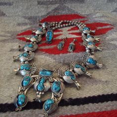 Big, Bold Squash Blossom Necklace Set featuring Rare Blue Diamond Turquoise comes with Navajo Rug as seen in photo. This necklace is so large and heavy it won't fit in any gift box, so we will wrap it up in the rug it's photographed on.  It also comes with gift boxes for the ring and earrings.  This set was in my mothers private collection and Tucson Silversmith, Alberto Contreras, created the ring to match the set. His hallmark is on the ring. The rare and vibrant Blue Diamond Turquoise stones have a black matrix and are beautifully matched in size and color. The contrasting color of the turquoise against the massive sterling silver pieces is striking.  We have not shined this up, we have let the patina of the silver shows it's age. Blue Diamond Turquoise is hard to find these days. This Blue Western Style Jewelry With Inlay, Southwestern Blue Jewelry For Wedding, Silver Squash Blossom Necklace, Navajo Rug, Diamond Mines, Navajo Rugs, Squash Blossom Necklace, Squash Blossom, Turquoise Stones