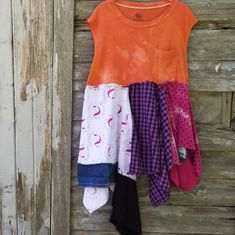 an orange shirt hanging on the side of a wooden wall with several different pieces of clothing