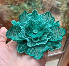 a hand holding a green brooch in front of a window