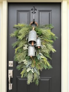 a christmas wreath with bells and evergreens on the front door is hanging from a black door